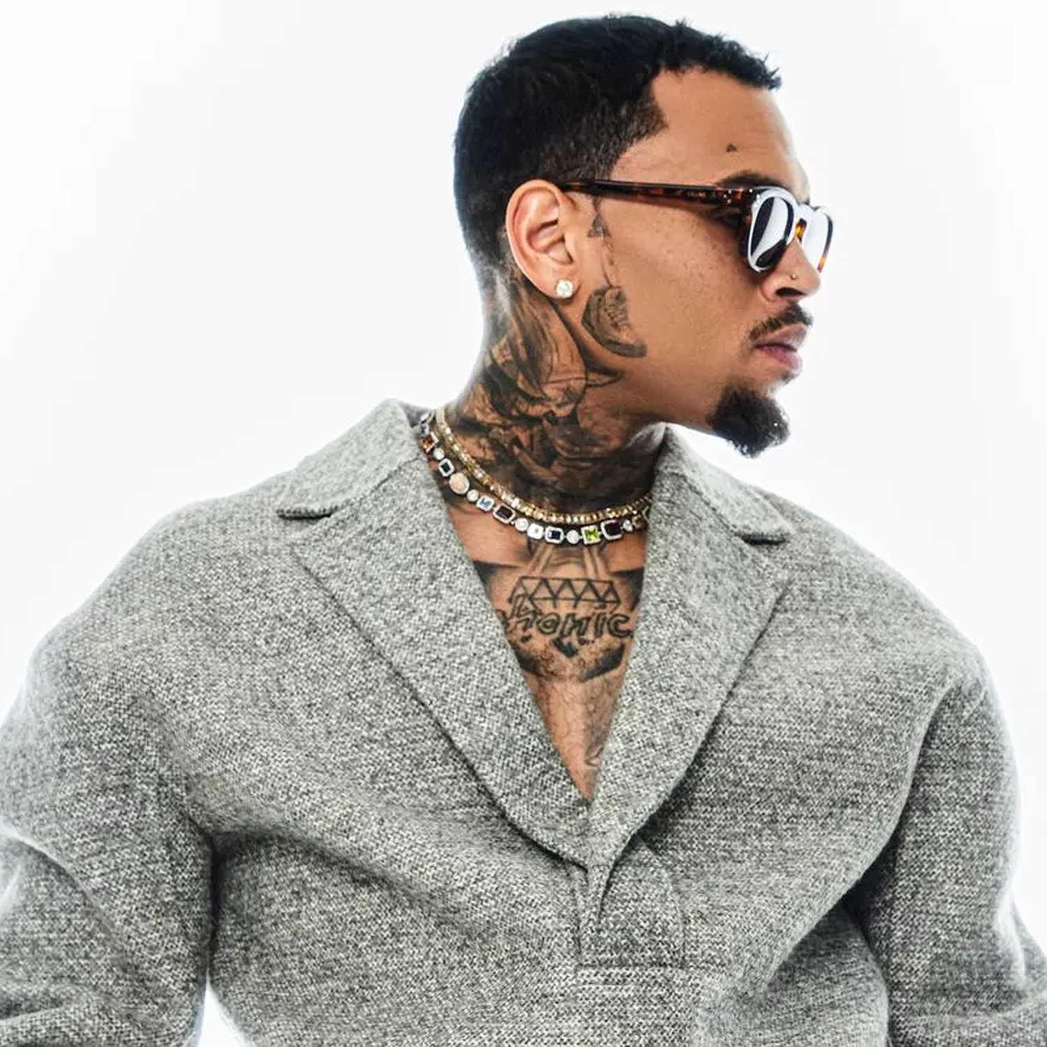 Man wearing a gray coat with tattoos visible on his neck and chest, against a white background